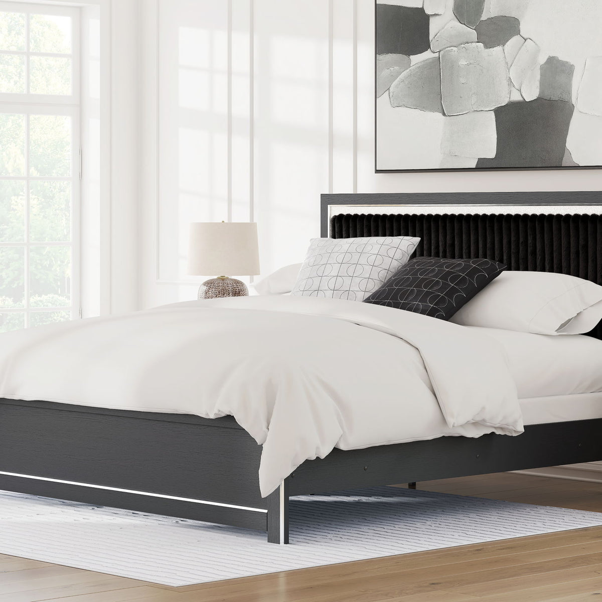 Upholstered panel bed with dark frame and upholstered headboard, shown with pillows and duvet.