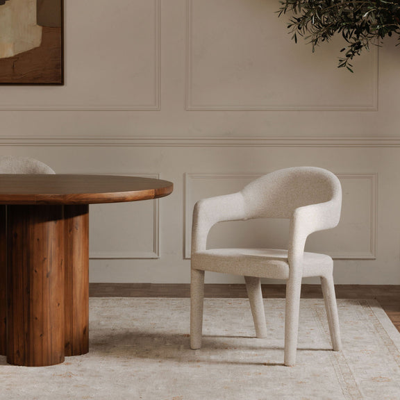 Beige upholstered dining chair with curved arms and tapered legs beside a dining table