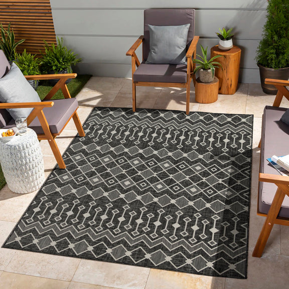 Indoor/outdoor polypropylene area rug, dark charcoal with white geometric line and diamond pattern.