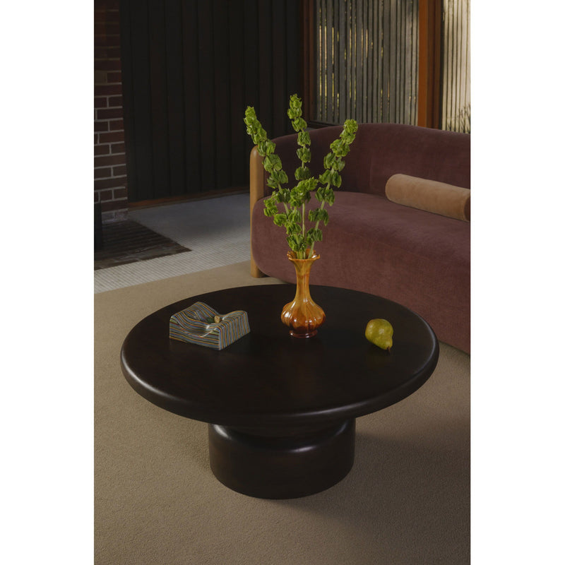 Brown round coffee table with pedestal base, plant vase and book on top