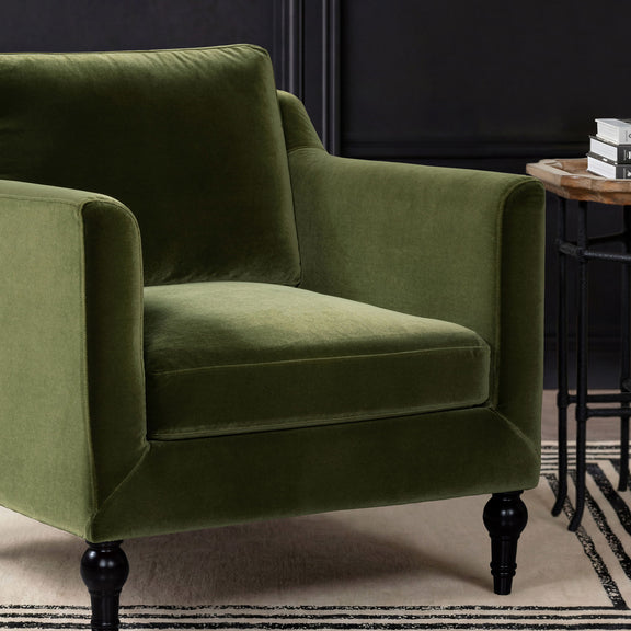 Green upholstered accent chair arm and seat detail with plush cushion and dark legs