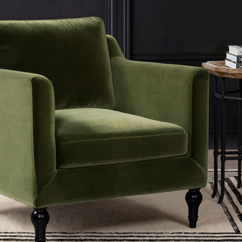 Green upholstered accent chair arm and seat detail with plush cushion and dark legs