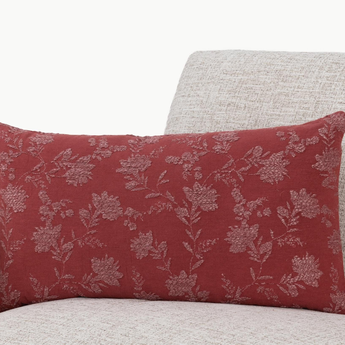 Burgundy red floral throw pillow with repeating vine and leaf pattern on textured fabric.