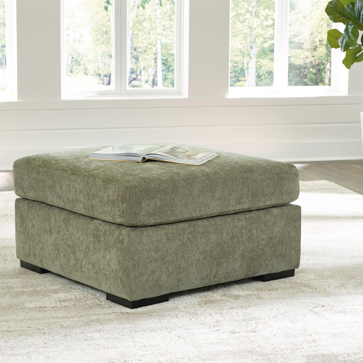 Oversized accent ottoman in green fabric with black legs and magazine on top
