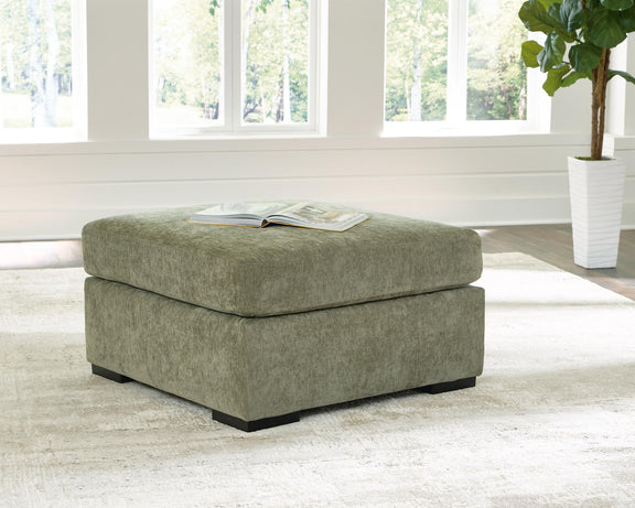 Oversized accent ottoman in green fabric with black legs and magazine on top