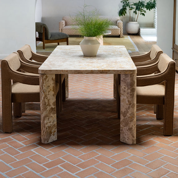 Dining table with beige stone-look top and pedestal base, surrounded by upholstered chairs