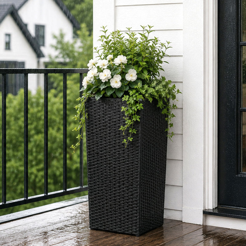 Tall black woven planter box filled with green foliage and white flowers