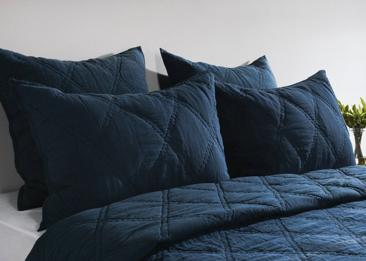 Blue quilted shams with diamond stitching on a bed