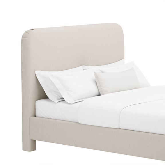 Light beige upholstered bed with rounded headboard, white pillows, and comforter