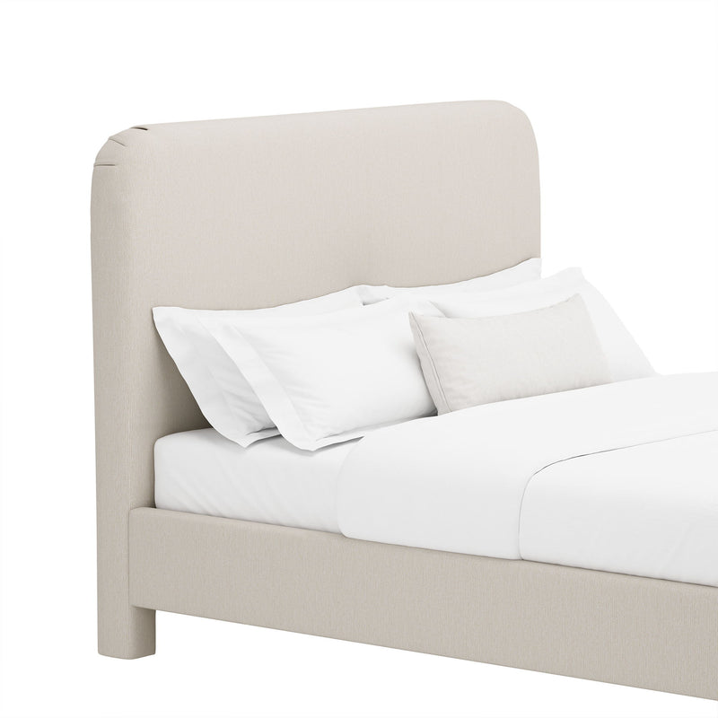 Light beige upholstered bed with rounded headboard, white pillows, and comforter