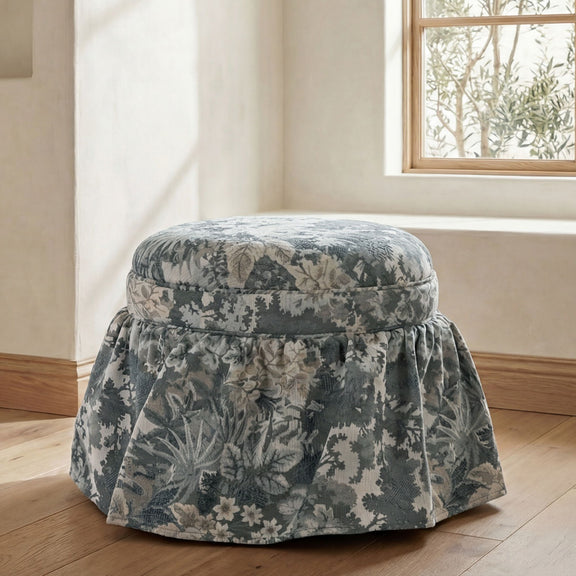 Round storage ottoman in blue-gray botanical tapestry with pleated, draped skirt