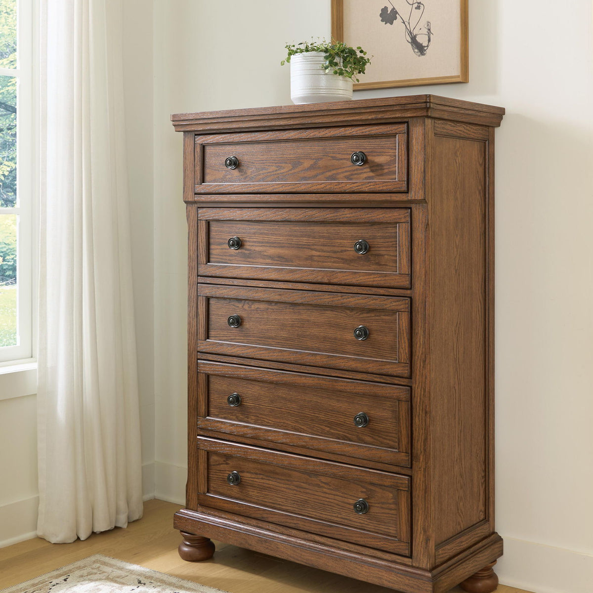Zackaryn warm brown wood five drawer chest with arched trim and round metal knobs, bun feet.