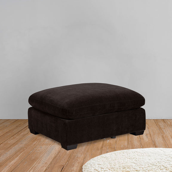 Dark brown upholstered ottoman with low legs and square padded sides.