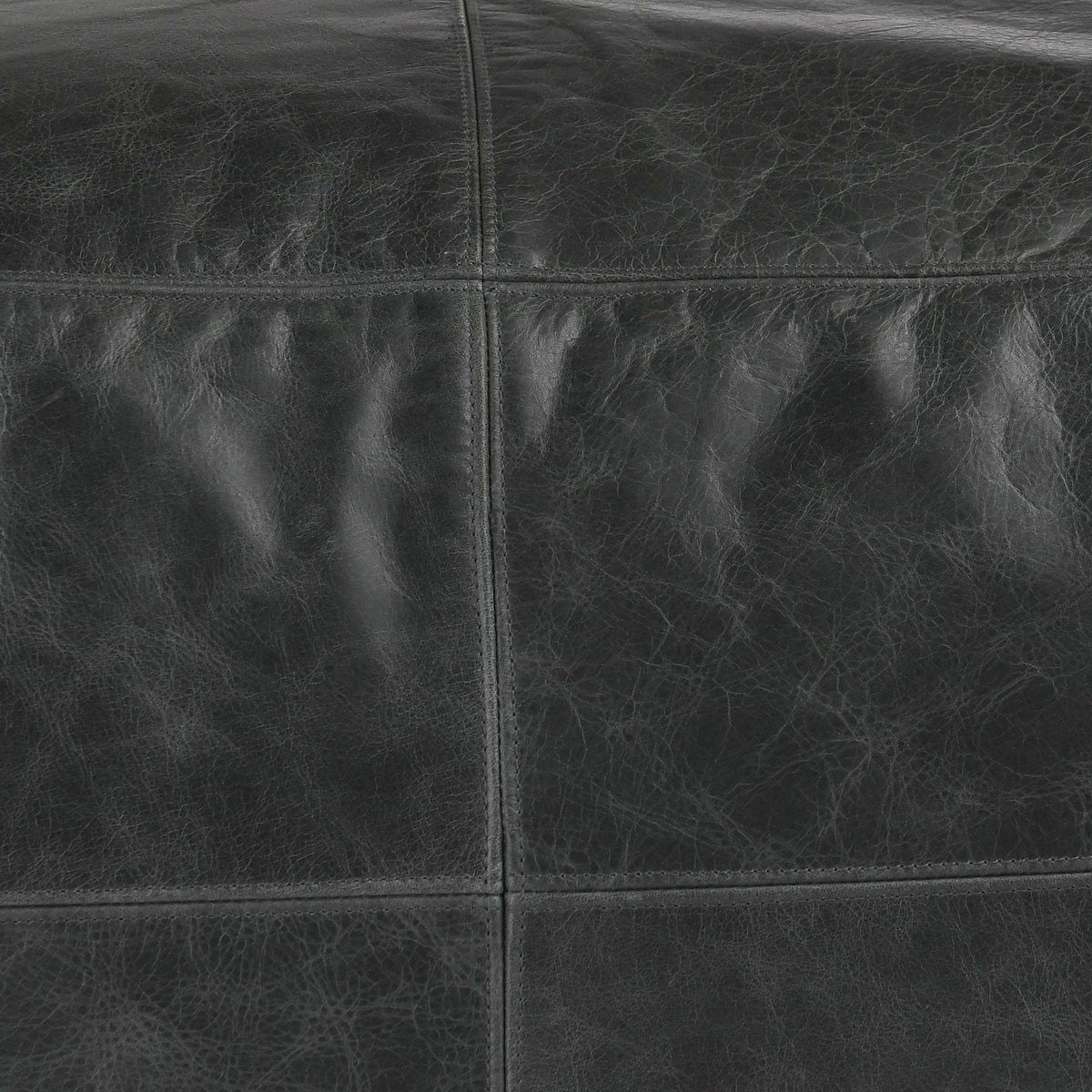 Close-up of onyx leather pouf seams and textured leather grain.