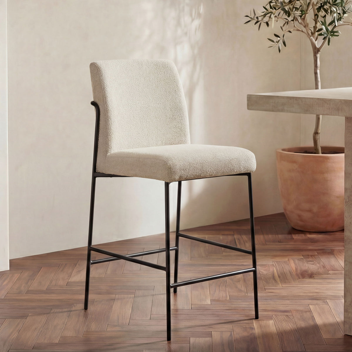 Ivory/beige fabric counter stool with curved back, black metal frame and lower bars.