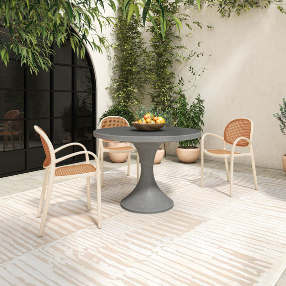 Outdoor dining table with round dark gray top and pedestal base, with chairs