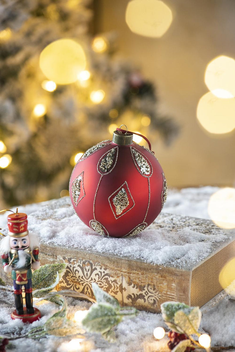 Red and gold decorative Christmas ball ornament on a snowy tabletop with nutcracker nearby