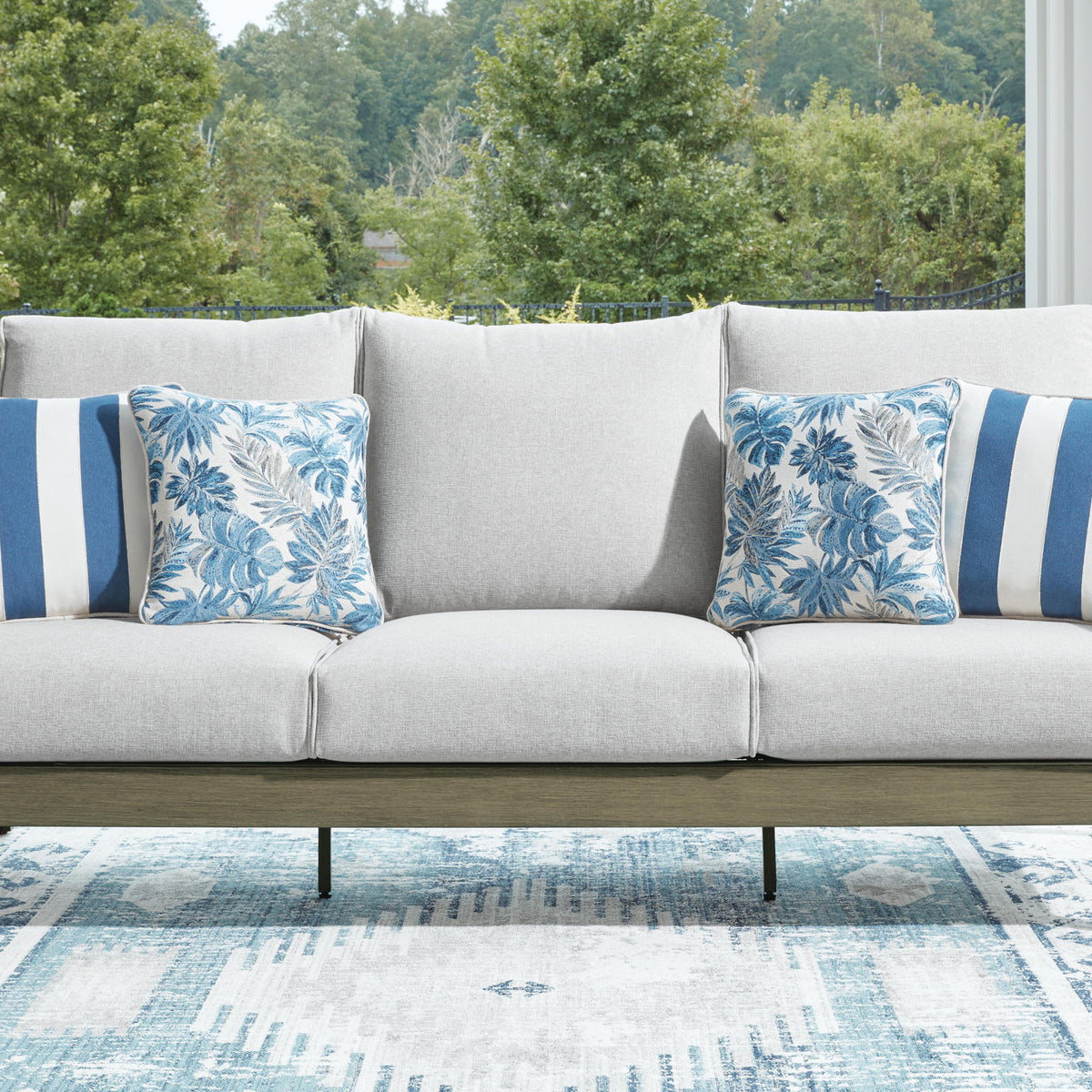 Gray sofa with brown frame, four blue patterned cushions and center lumbar pillow