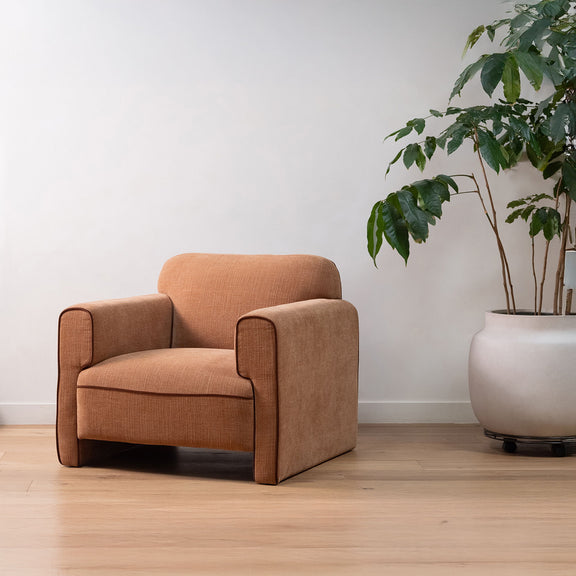Light brown upholstered armchair with wide track arms and boxy seat-back.