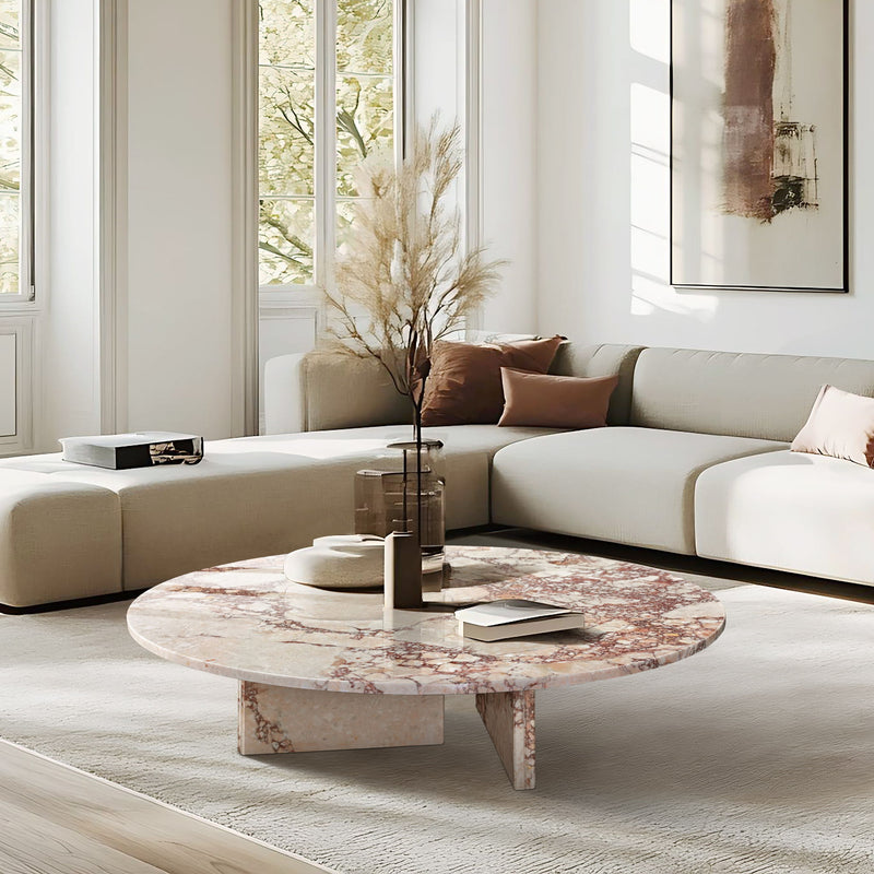 Round marble-look coffee table with pink-beige veined top and stone pedestal base