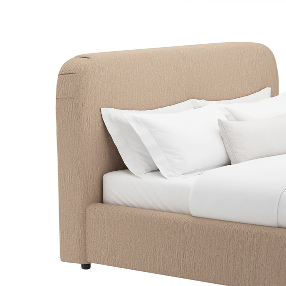 Light brown upholstered bed headboard with white pillows and bedding