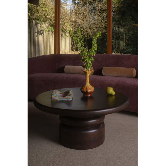 Brown round coffee table with pedestal base, vase and lemons on tabletop