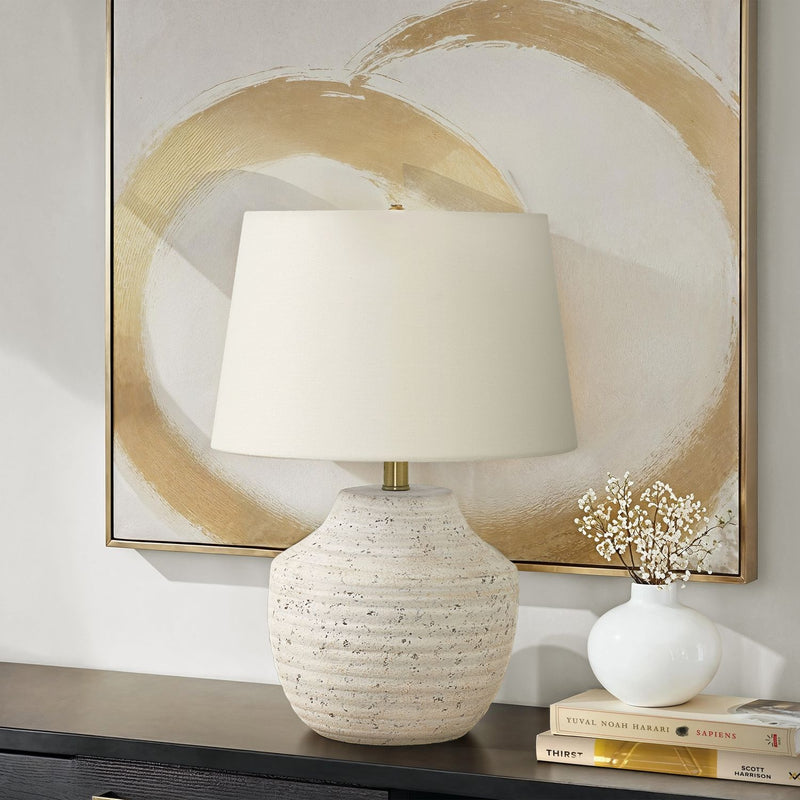 Table lamp with cream speckled concrete base, brass neck, and off-white drum shade