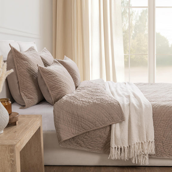 Beige velvet bedding set with matching pillows and fringed throw on bed