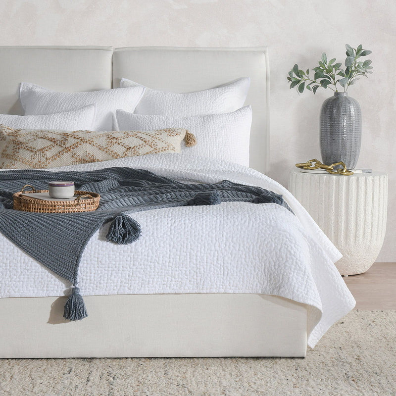 Quilt set bedding with white quilt, layered shams, and a gray tassel accent