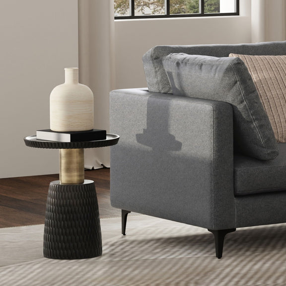 Black and gold pedestal side table beside a sofa, shown holding a vase and books.