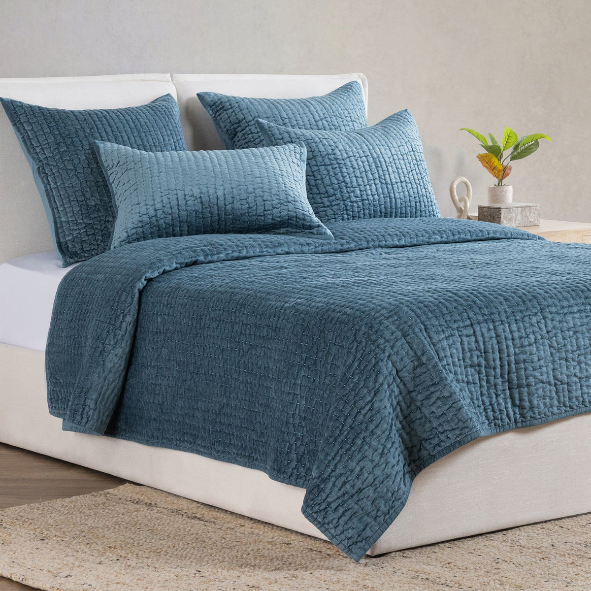Blue velvet quilt set with textured quilt and matching shams on a bed