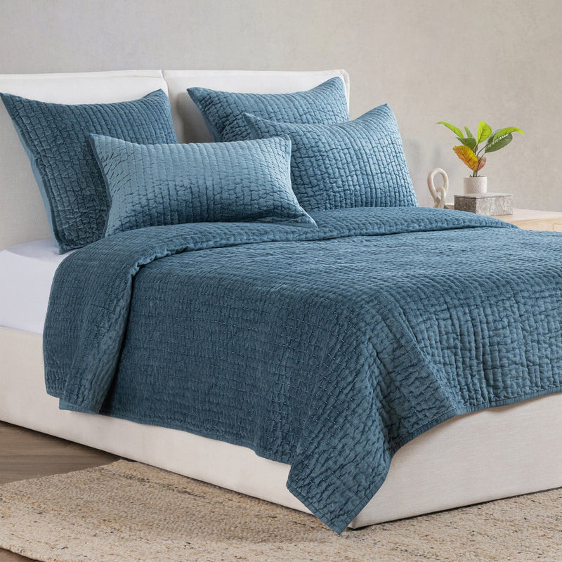 Blue velvet quilt set with textured quilt and matching shams on a bed