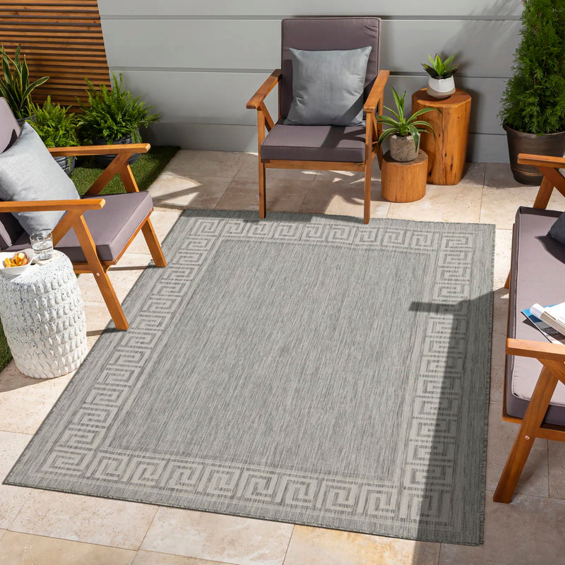 Indoor/outdoor area rug in light gray with Greek key border pattern on patio