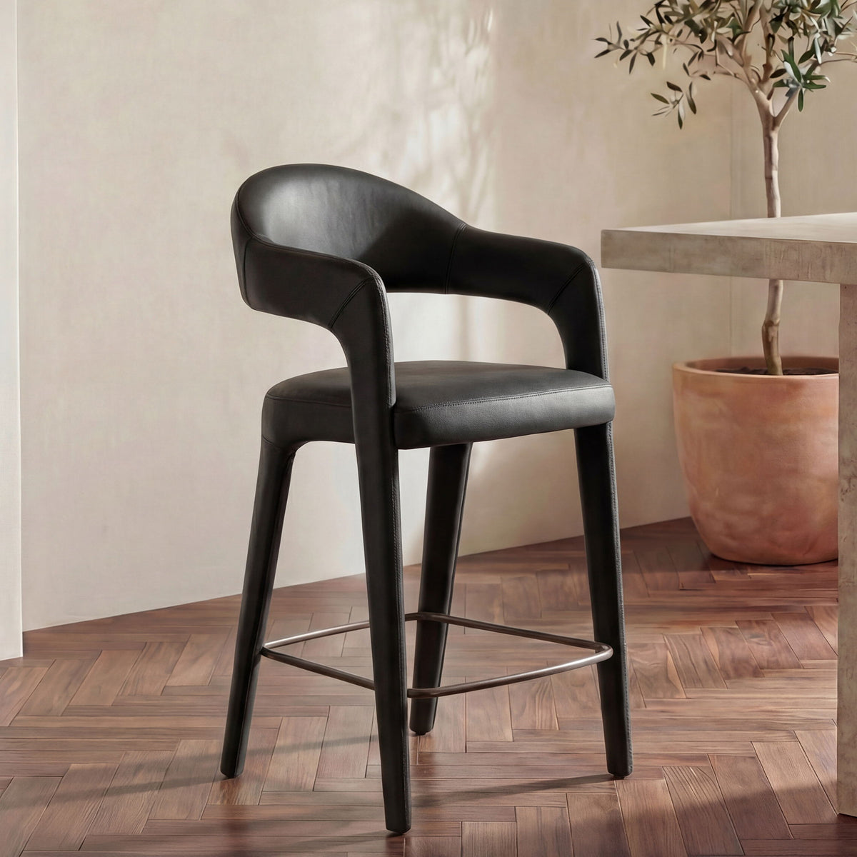 Black leather counter stool with curved arms, cushioned seat, and metal footrest