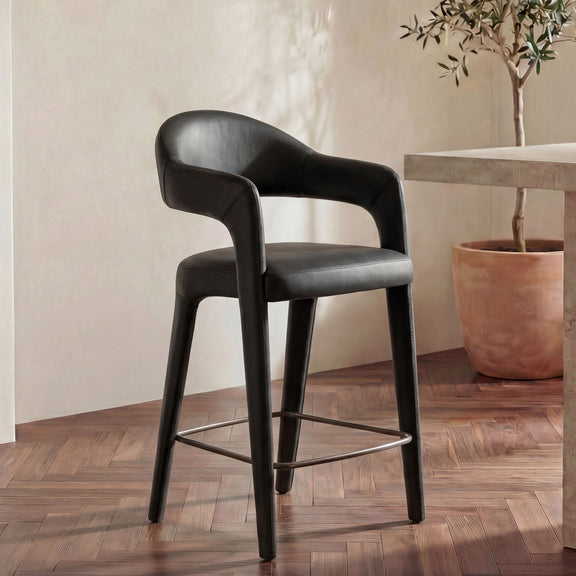 Black leather counter stool with curved arms, cushioned seat, and metal footrest