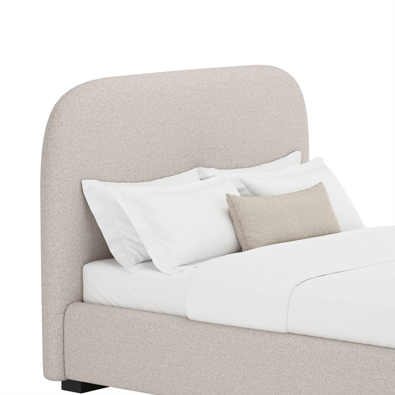 Light gray upholstered bed with rounded headboard and side panel, styled with pillows