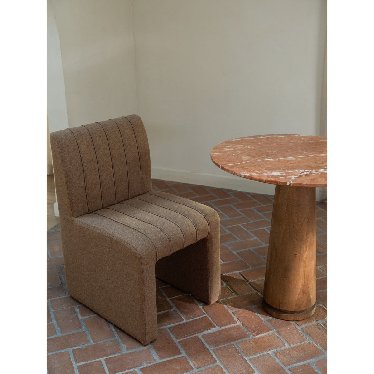 Light brown upholstered dining chair with channel back, wide seat, and curved arms