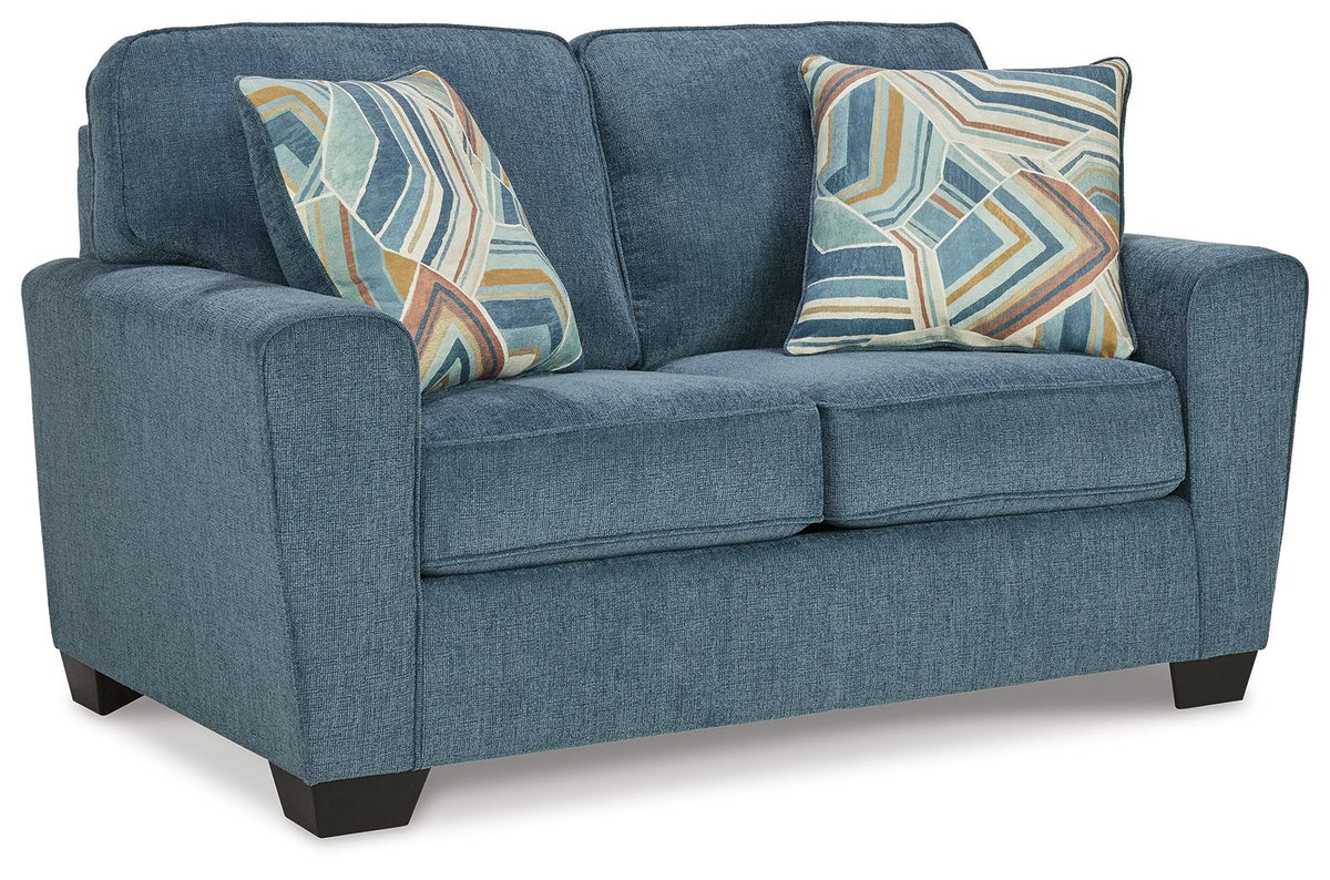 Blue fabric loveseat with two geometric patterned throw pillows and rolled arms