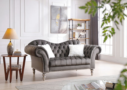 Dark gray tufted round arm loveseat with studded trim and two white faux fur pillows.