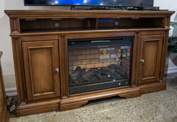 Brown wooden TV stand with two cabinet doors and built-in fireplace insert