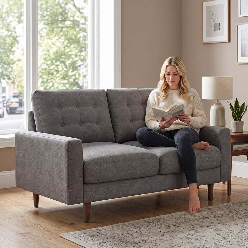 Dark gray tufted two-seat loveseat sofa with a person seated on one cushion