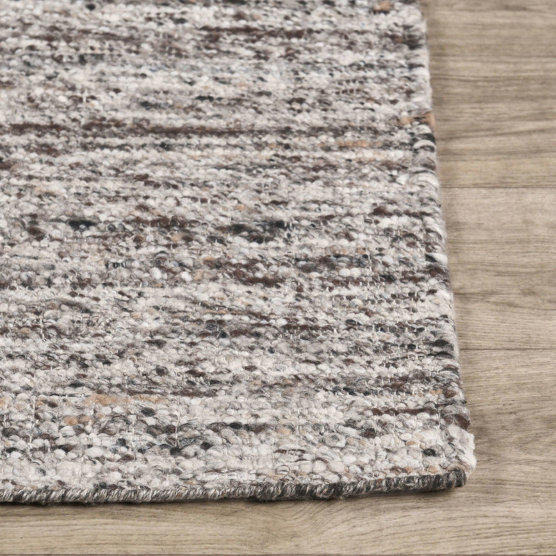 Close-up corner of tan speckled area rug with textured pile and bound edge.