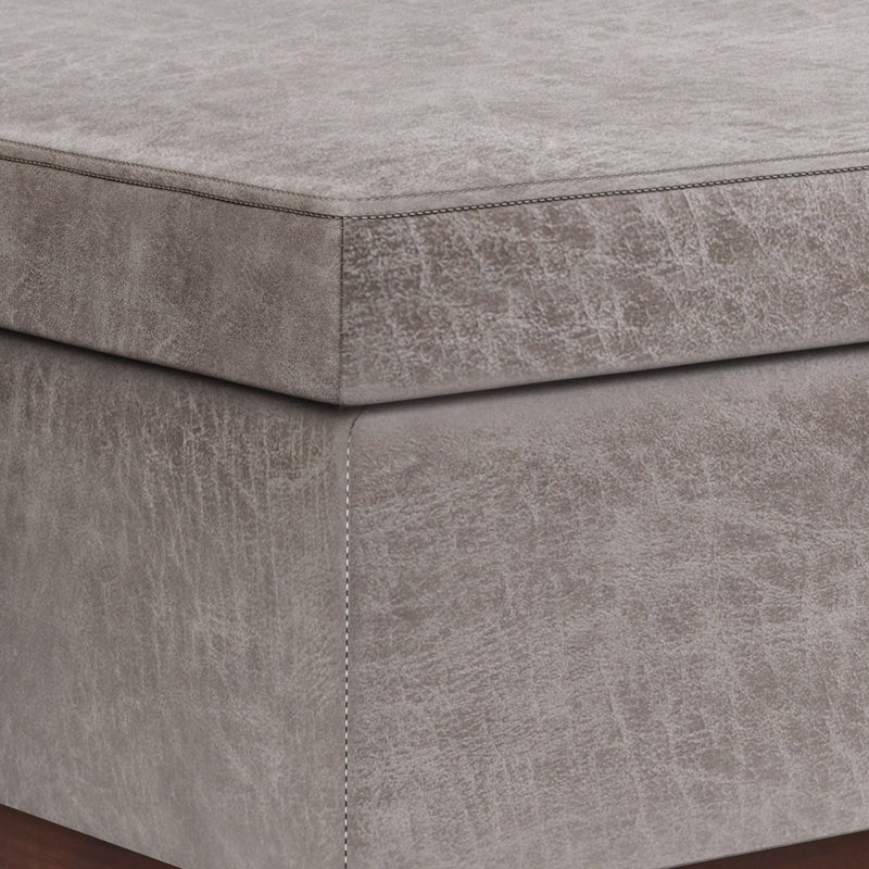 Gray faux leather storage ottoman with visible seams along the lift-top side