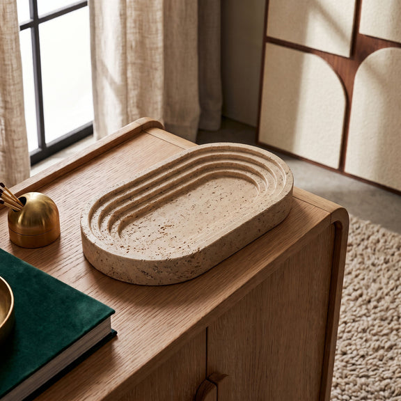 Oval travertine marble tray with raised rim and natural speckled beige pattern.