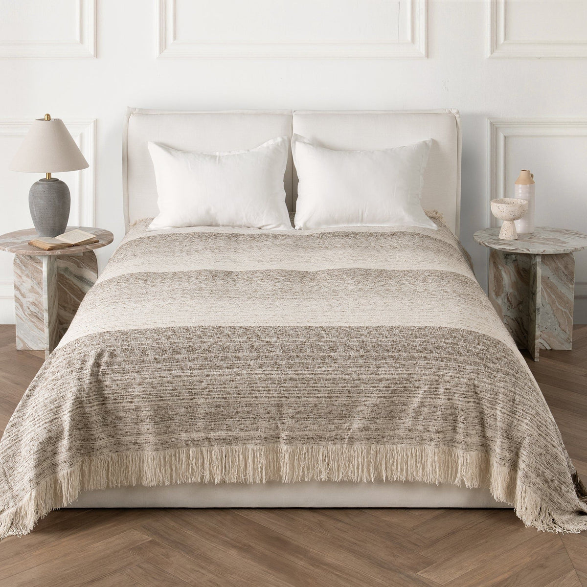 Woven throw blanket on bed, neutral base with speckled pattern and fringed hem