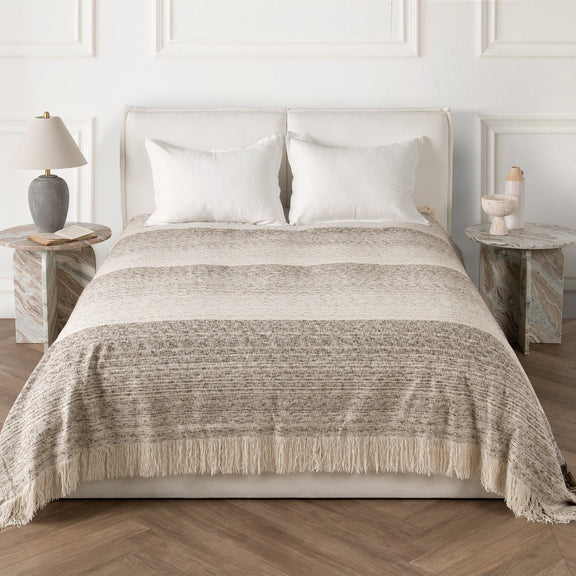 Woven throw blanket on bed, neutral base with speckled pattern and fringed hem