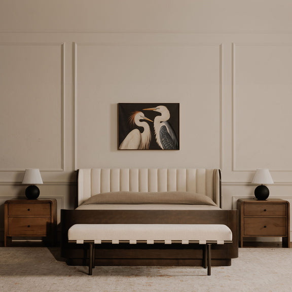 Beige upholstered dining bench with a cushioned seat and slim dark legs, shown at the foot of a bed