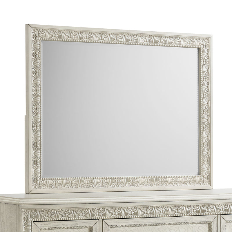Ornate white mirror with carved frame on top of a dresser.
