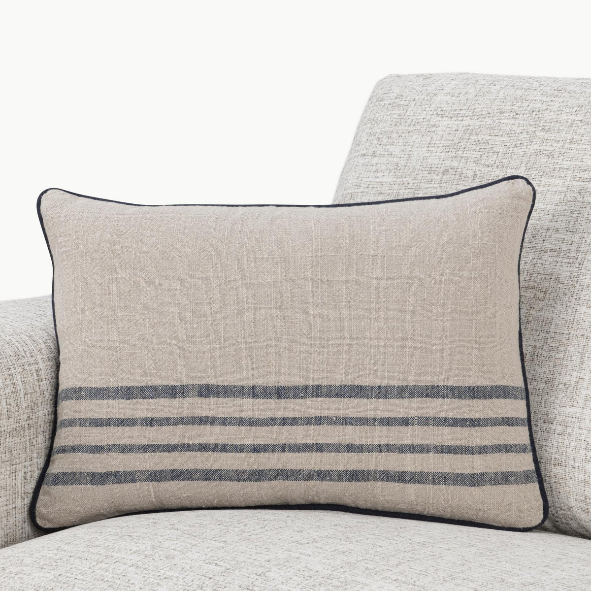 Natural linen throw pillow with blue horizontal stripes and dark piped edge on sofa.
