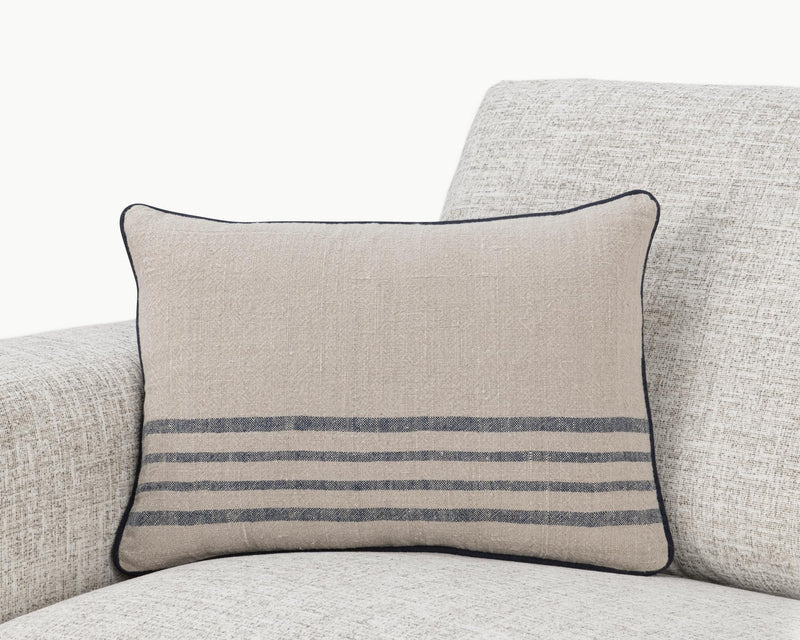 Natural linen throw pillow with blue horizontal stripes and dark piped edge on sofa.